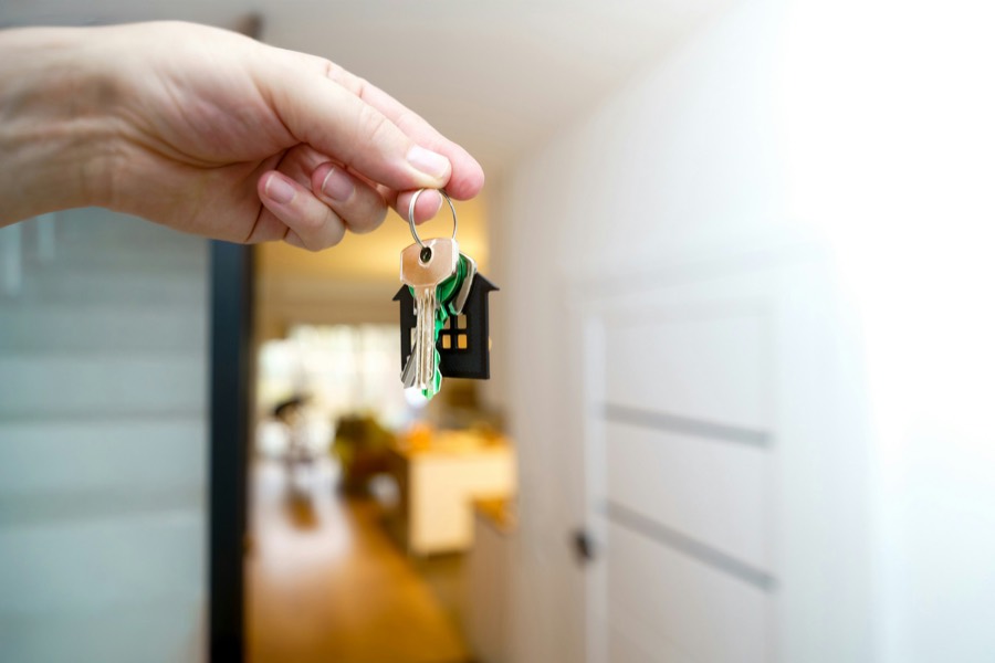 Hand hält Wohnungsschlüssel mit Haus-Anhänger im Eingangsbereich einer hellen Wohnung